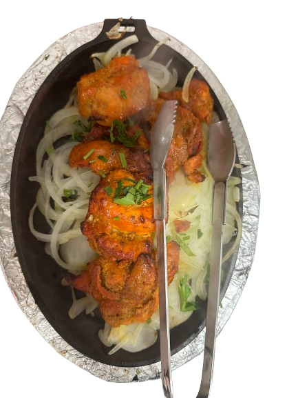 A tray of chicken tikka with onions underneath, accompanied by a kabab spoon.