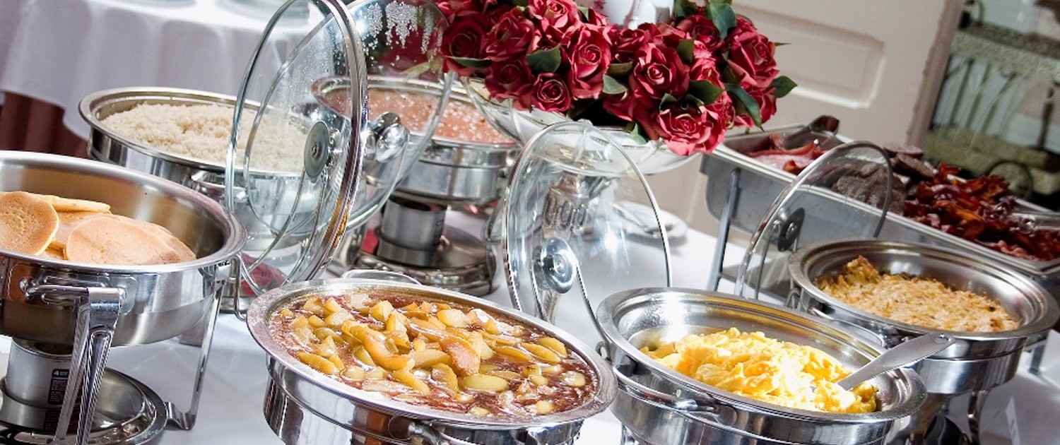 Various food items displayed on a buffet table, accompanied by dishes and a flower vase